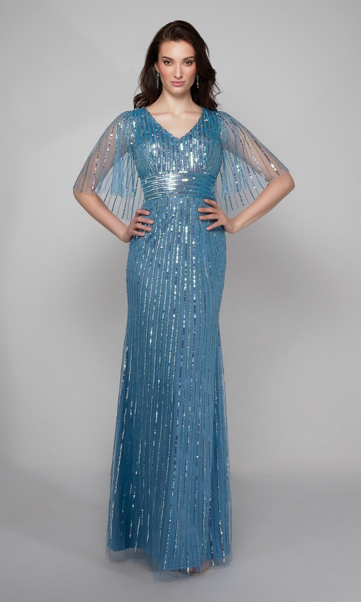 A woman faces forward wearing the Alyce 27599 long formal dress in Niagara Blue with beaded sequins and short sheer sleeves, standing against a plain gray background—a stunning choice for a mother-of-the-bride look.